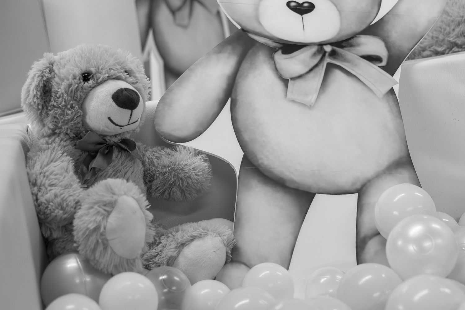 Two teddy bears, one small fluffy and one large, surrounded by white balls in a black and white photo.