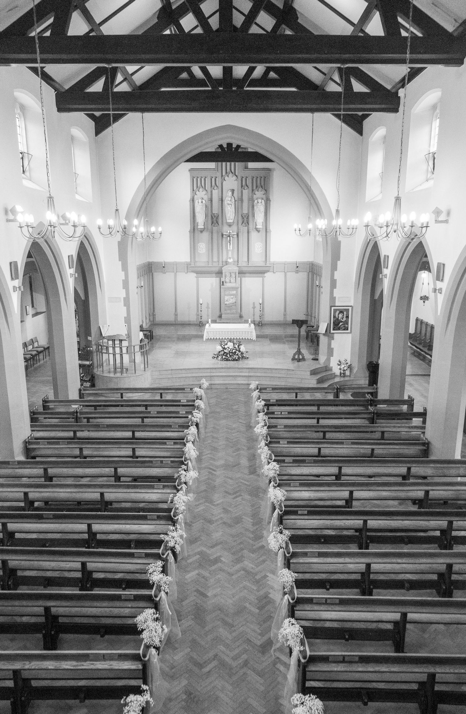 Empty church interior with wooden pews and decorative floral arrangements along the aisle.