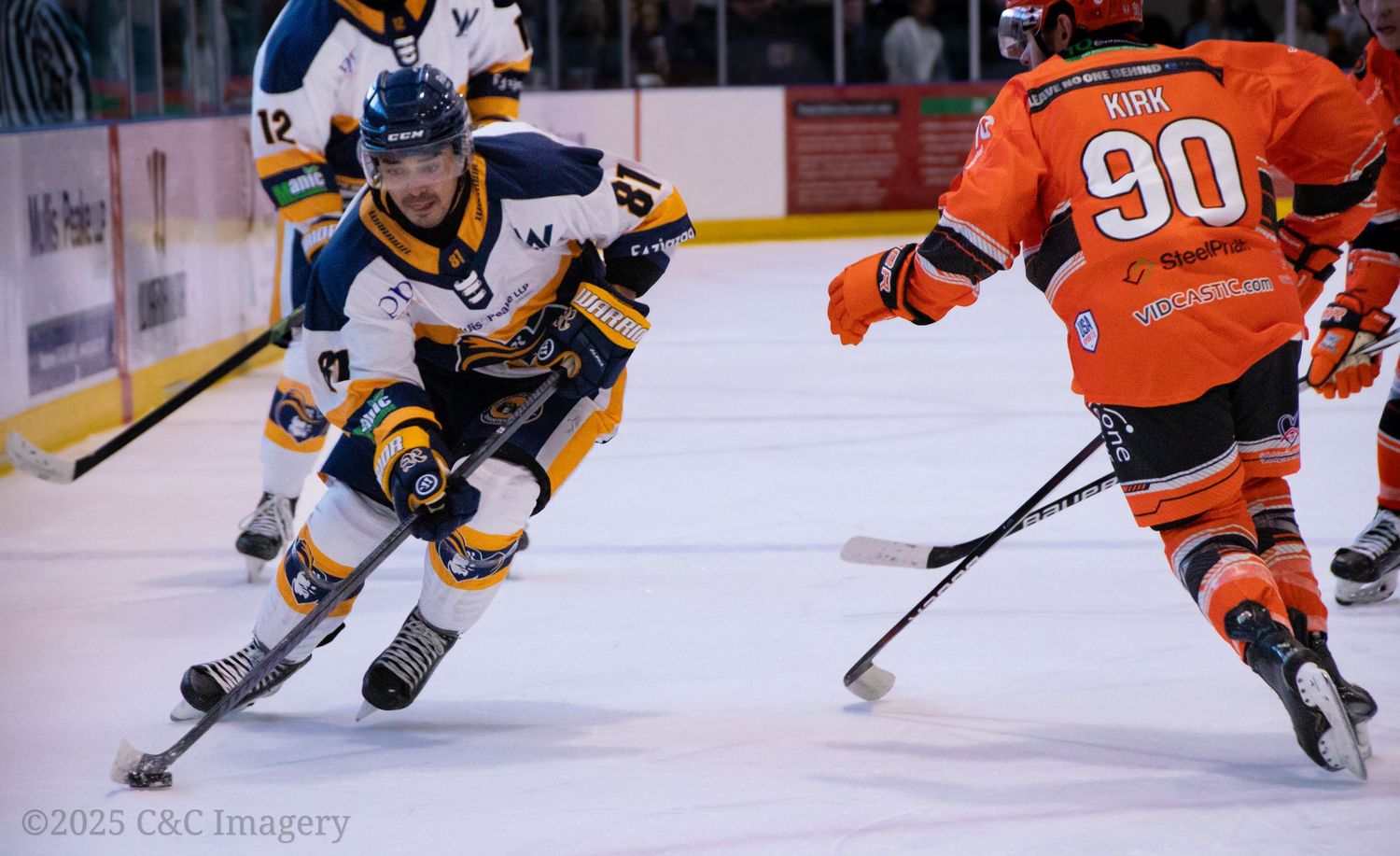 Ice hockey players in orange and yellow jerseys battle for the puck during an intense game.