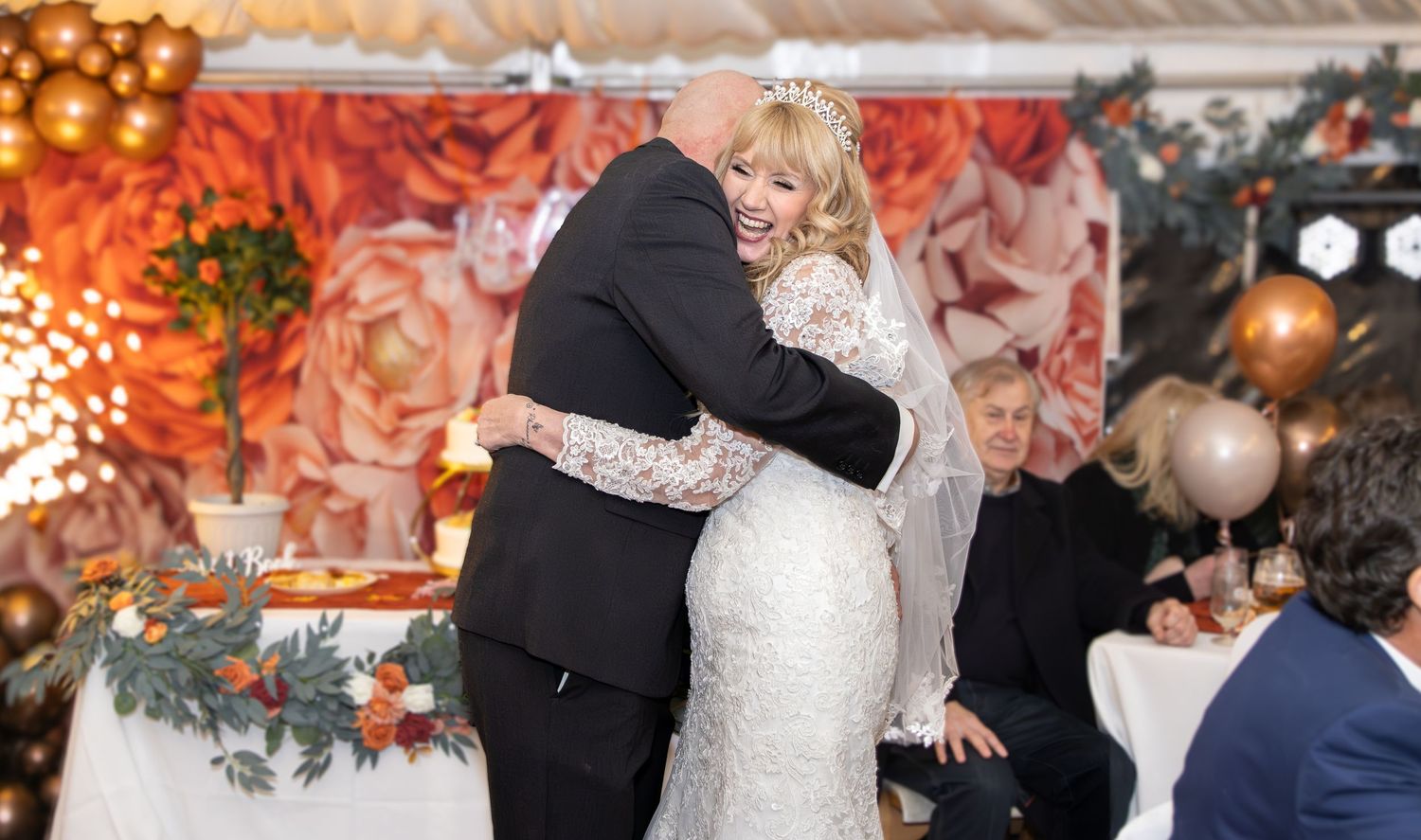 Wedding couple shares a romantic dance on an elegantly decorated ballroom floor with warm lighting and floral decor.