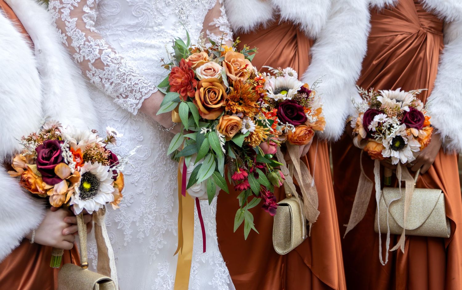A row of bridesmaids bouquets with autumn colors and dried flowers lined up against a rust-colored backdrop.