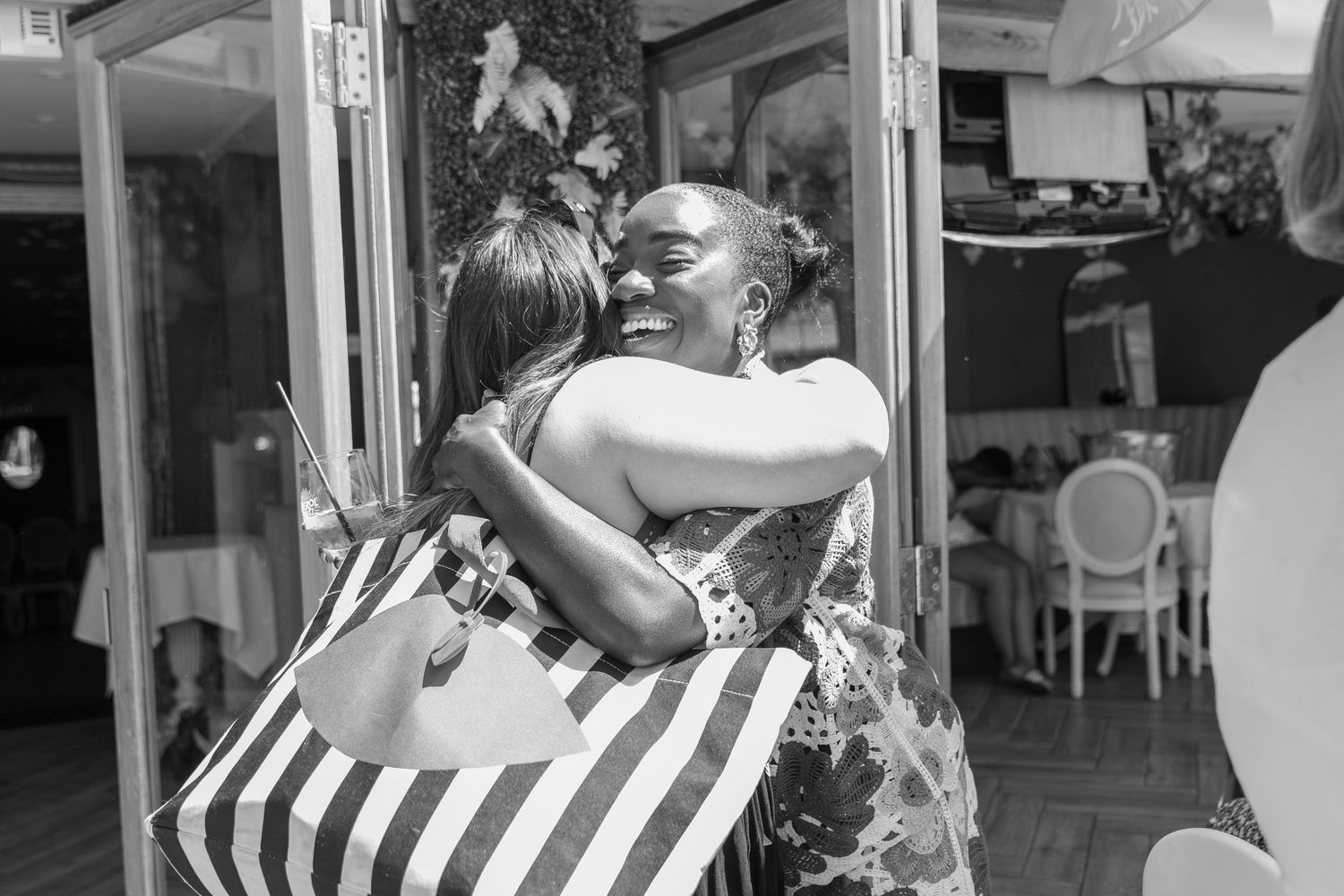 Two women share a warm embrace outside a restaurant in this black and white photo.