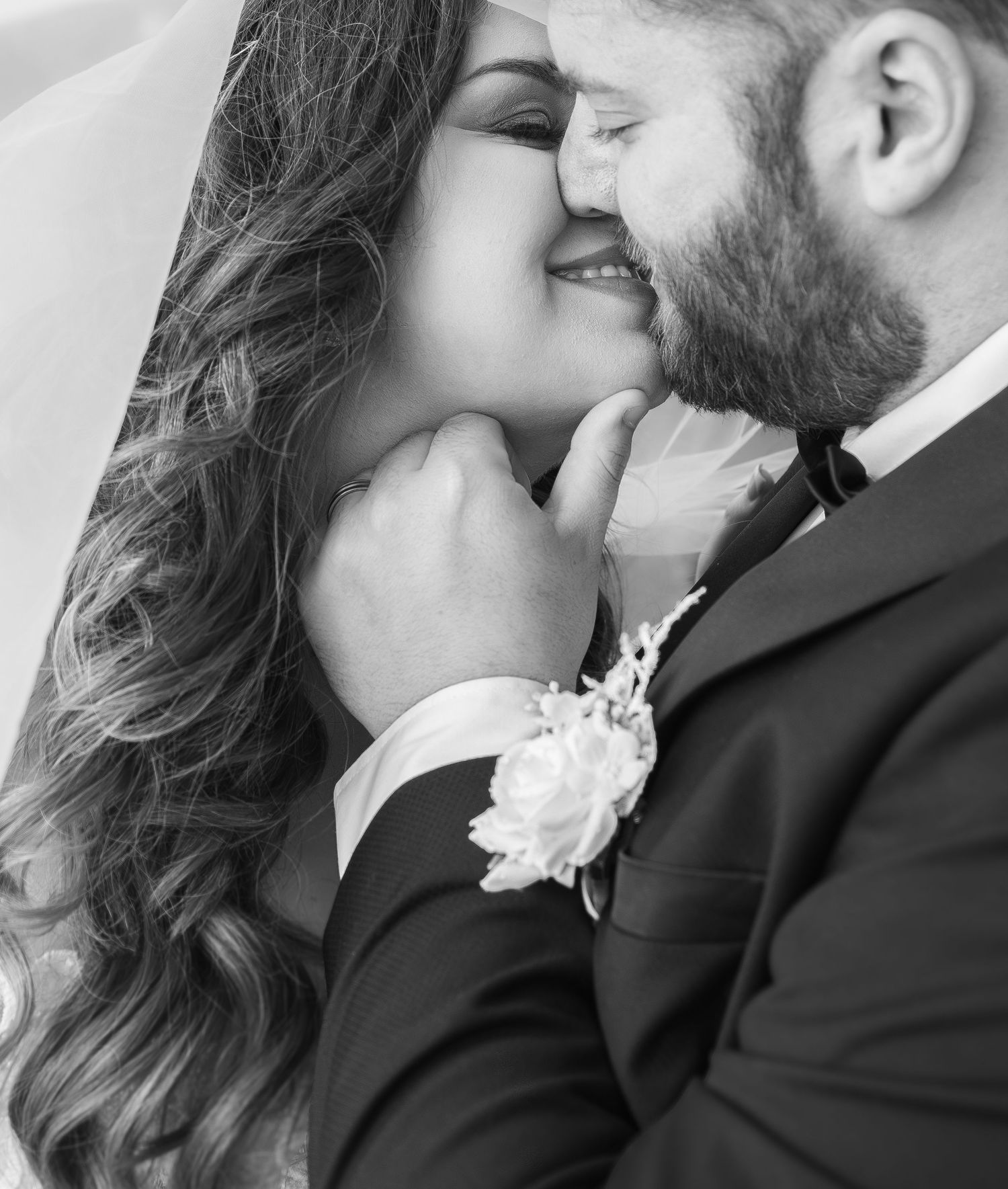Black and white wedding photo of bride and groom sharing an intimate moment, groom wearing boutonniere suit.