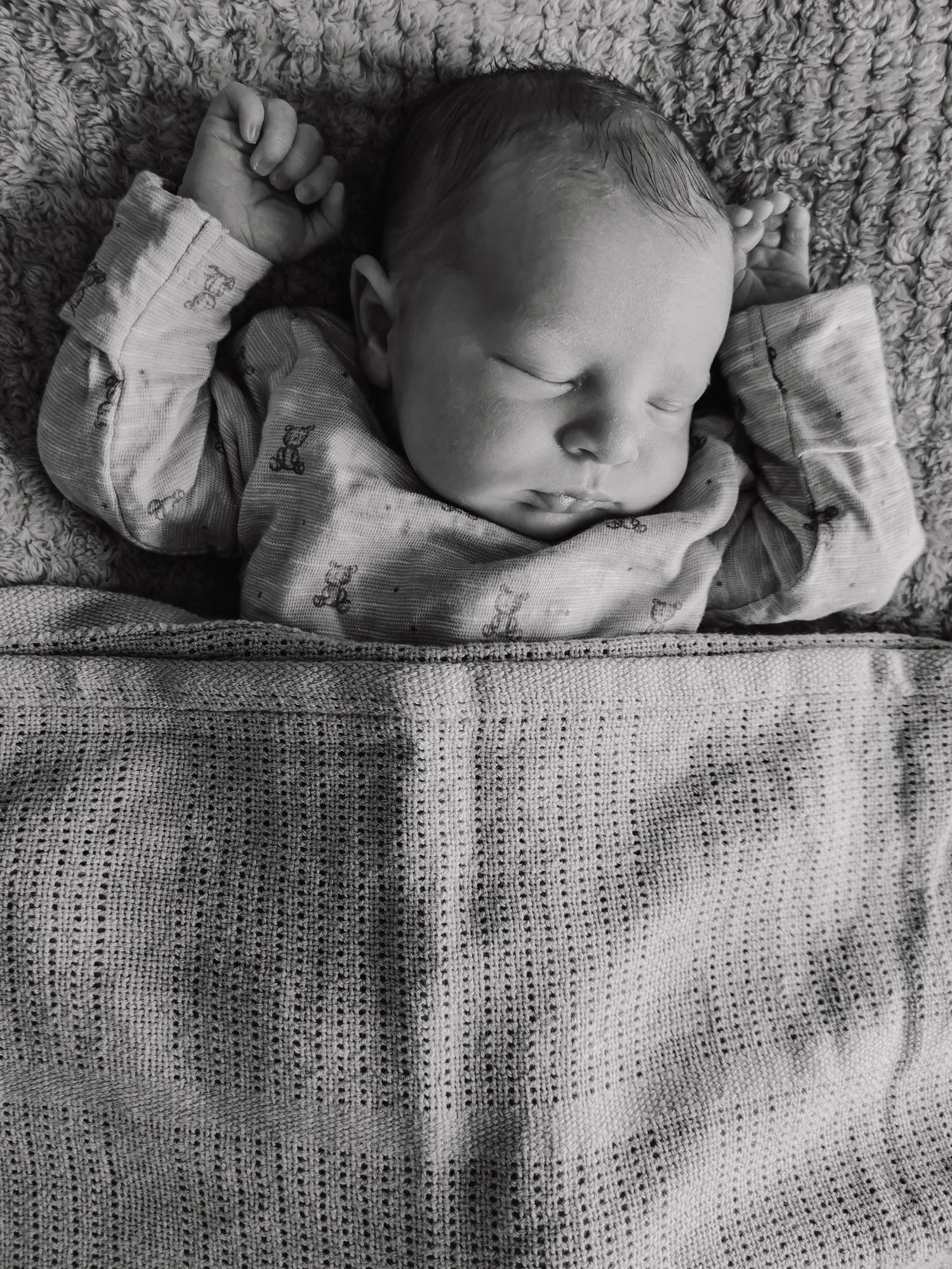 Black and white photo of a sleeping newborn baby wrapped in a knit blanket.