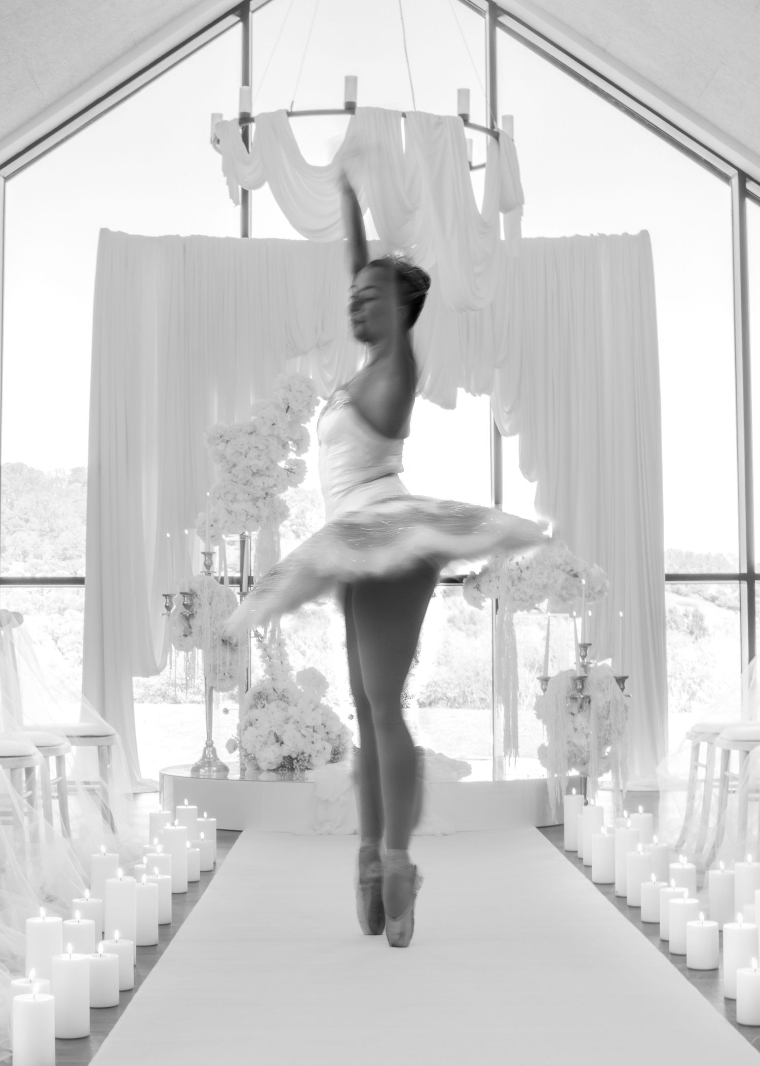 Black and white photo of a ballerina in tutu dancing en pointe in an elegant wedding venue with candles and floral decor.
