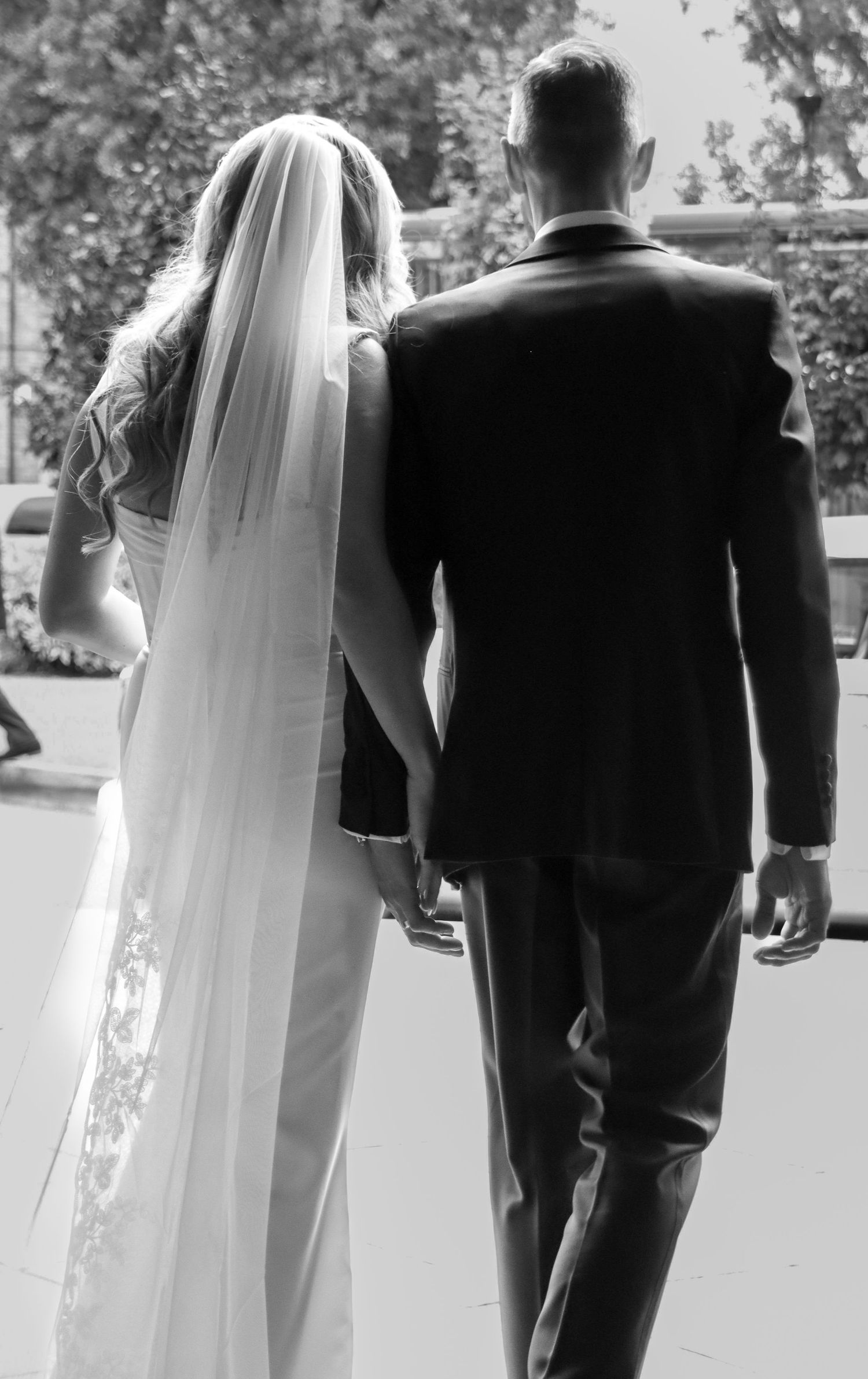 Back view of newlyweds walking together, bride in white dress with veil and groom in dark suit.