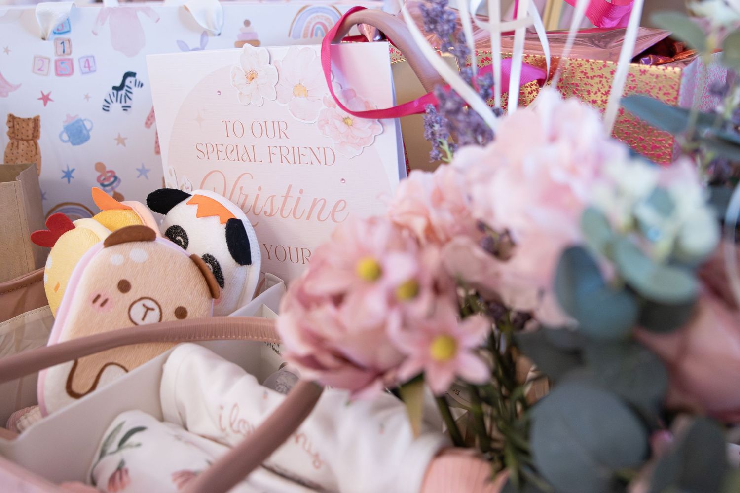 Pink flowers and stuffed animals surround a greeting card addressed to Christine at a baby shower celebration.