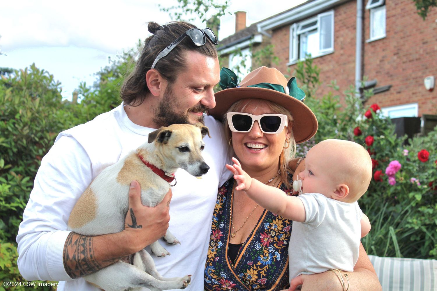 Family poses together with their small dog in a garden setting.