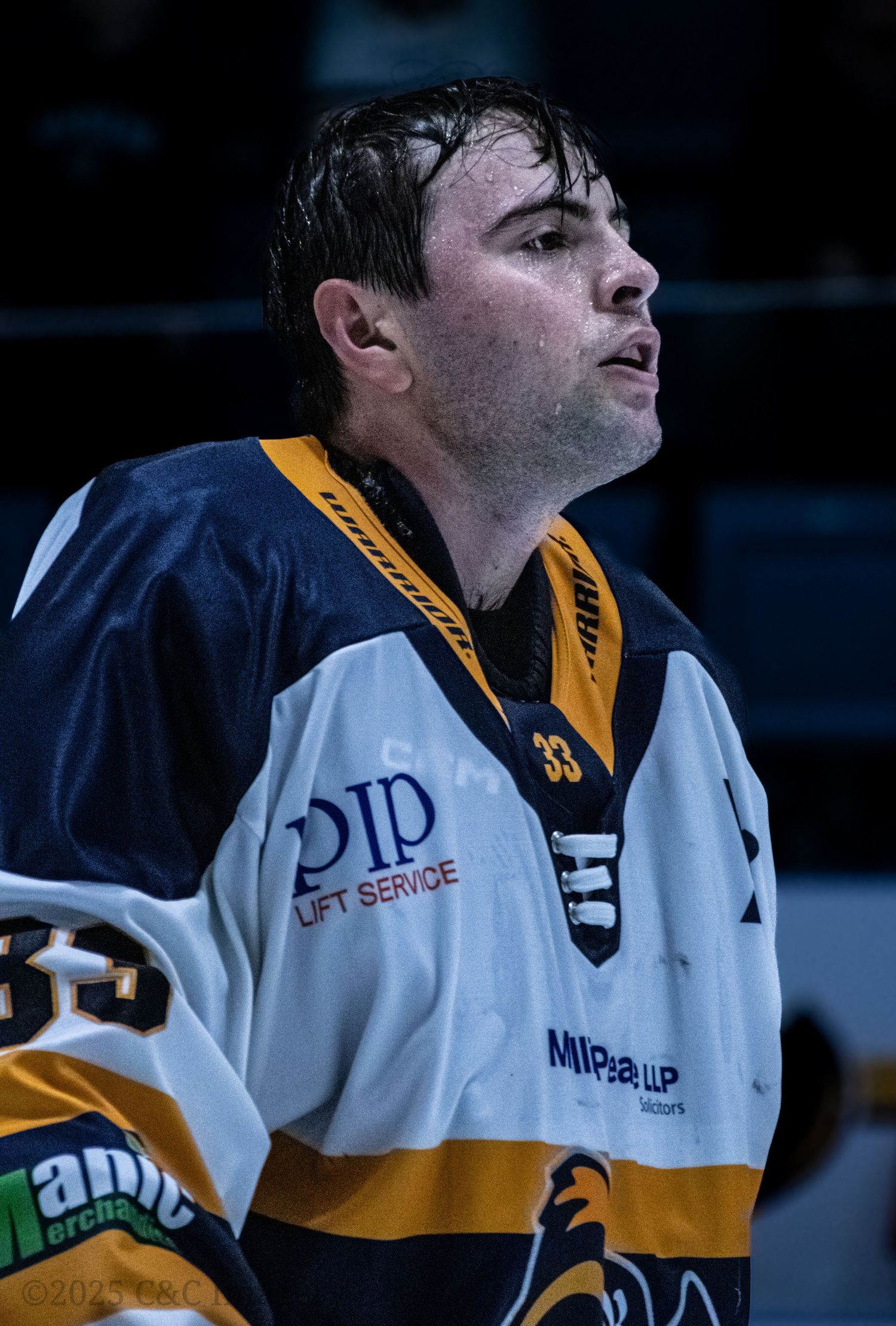 Hockey player in white and yellow uniform shows intensity during game break.