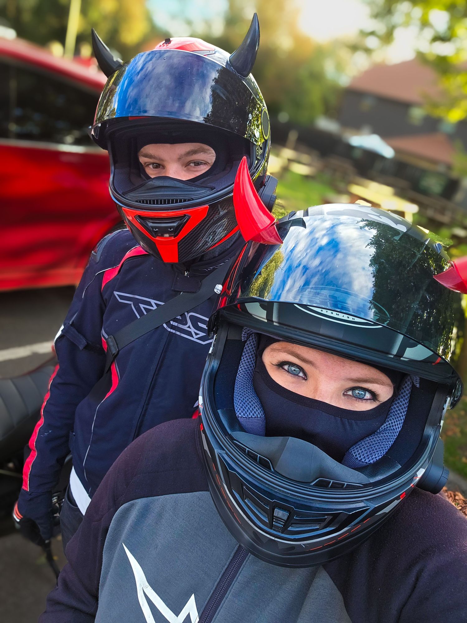 Two people wearing protective motorcycle helmets posing together outdoors.