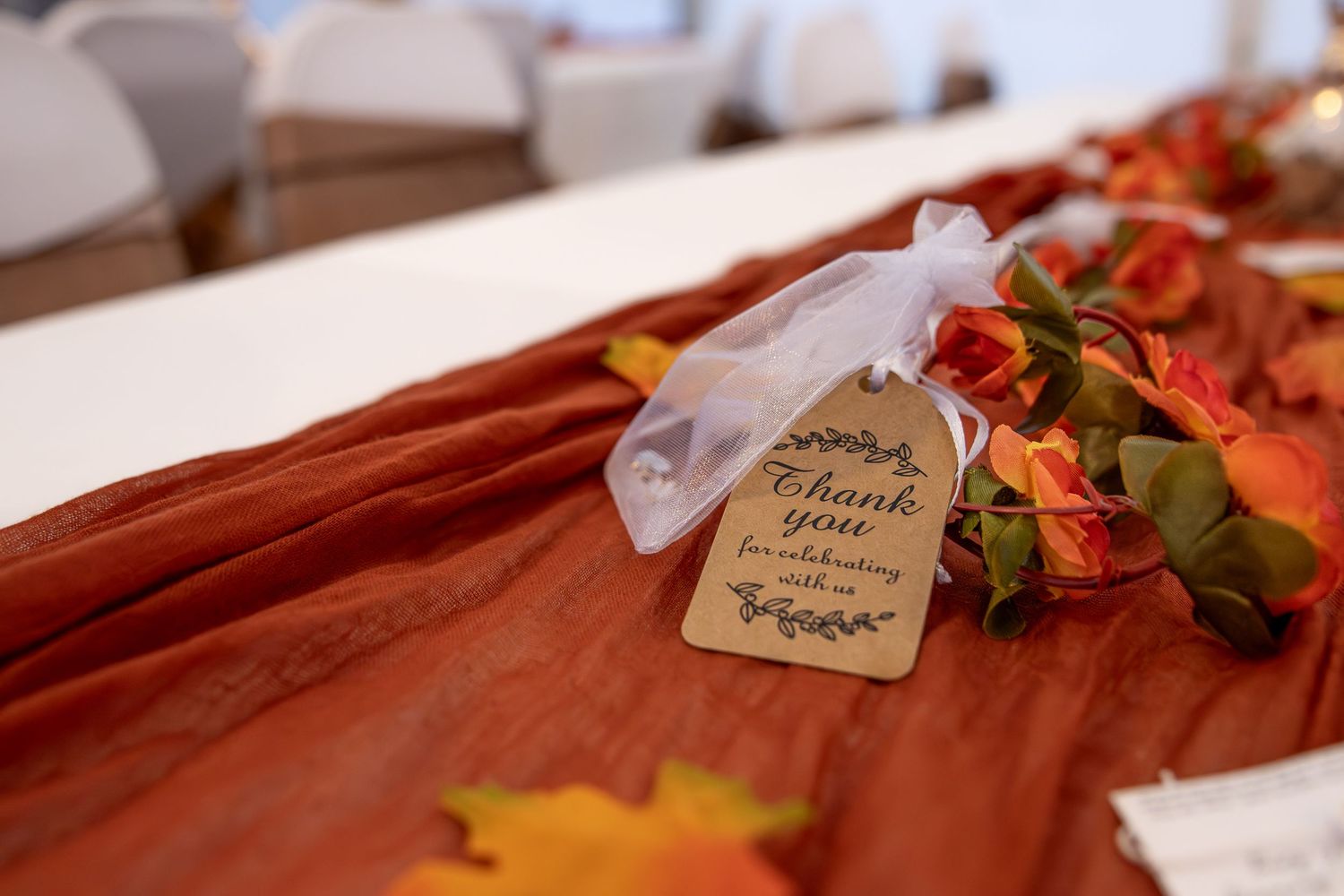 A handwritten thank you note tag with autumn leaves and orange fabric in soft focus background.