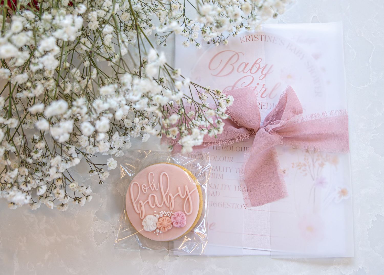 Pink baby shower cookie and invitation card with floral decorations and baby girl theme on white background.