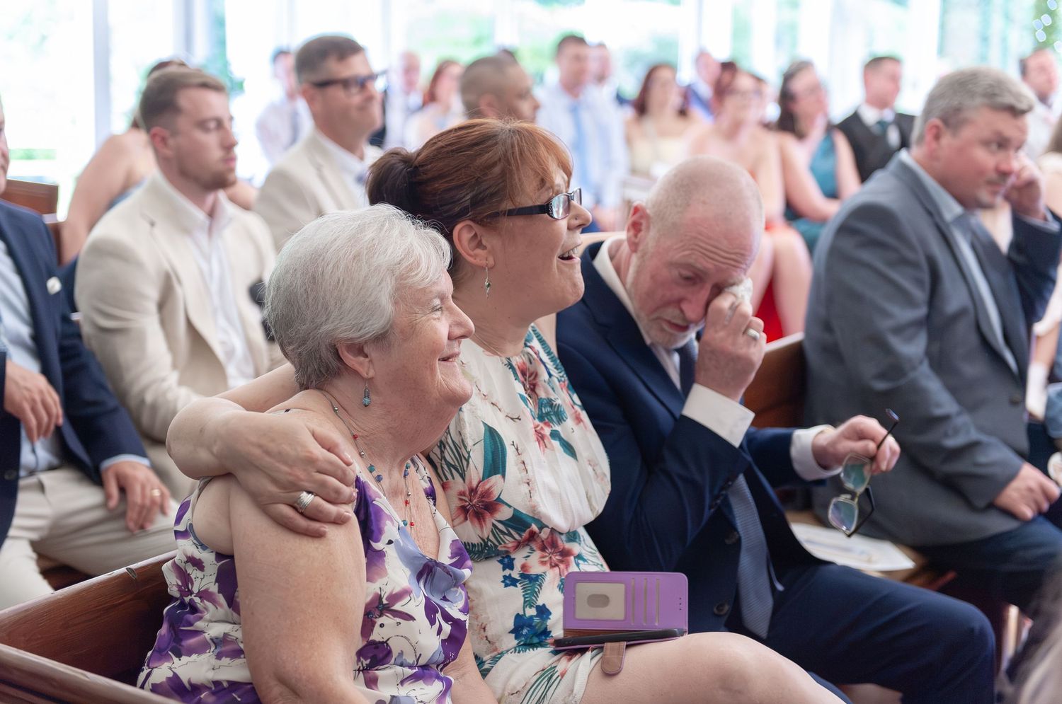 Emotional wedding guests laughing and crying during an outdoor ceremony, seated in rows at a summer celebration.