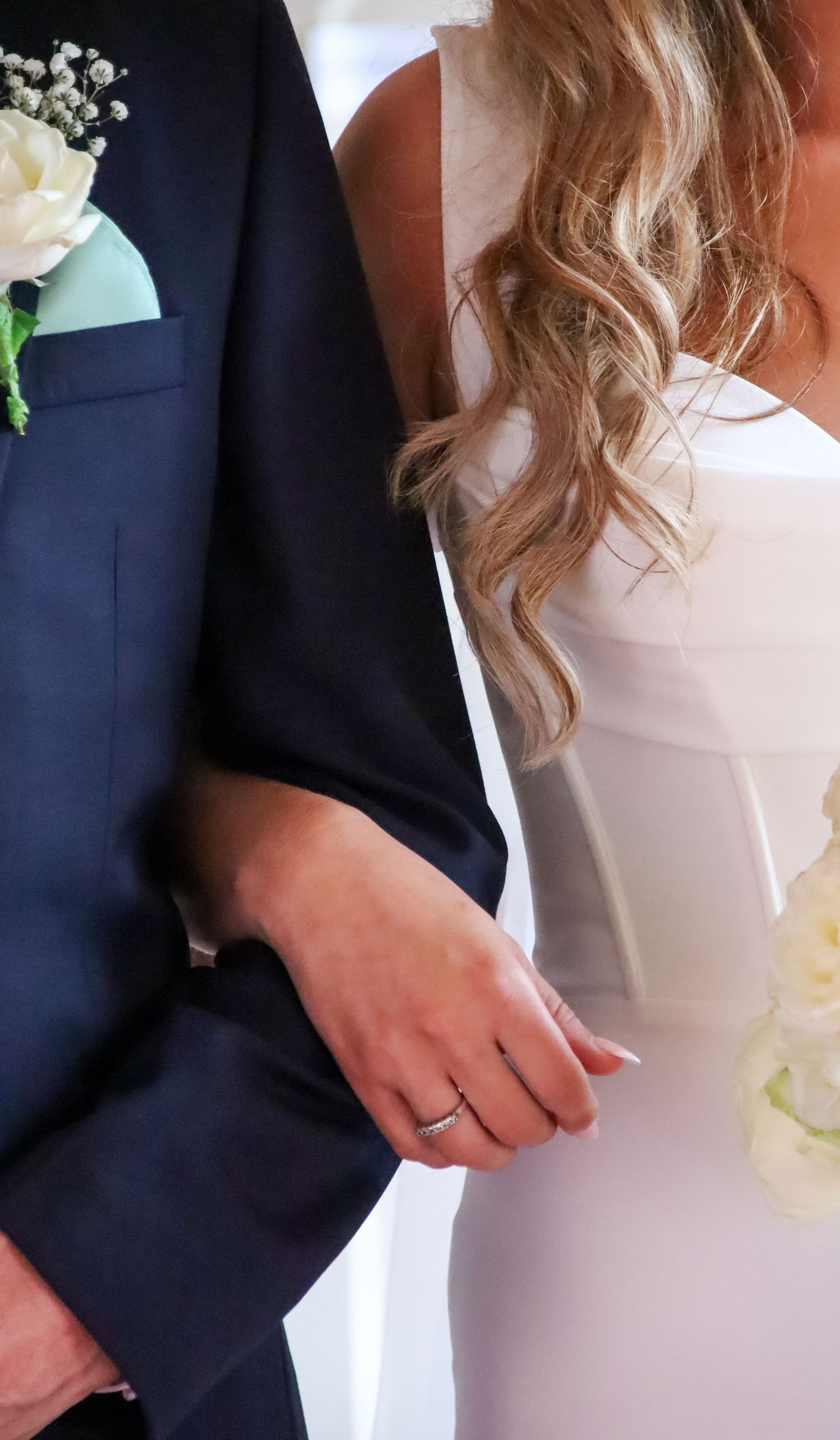 Detail shot of navy suit with boutonniere next to white wedding dress.