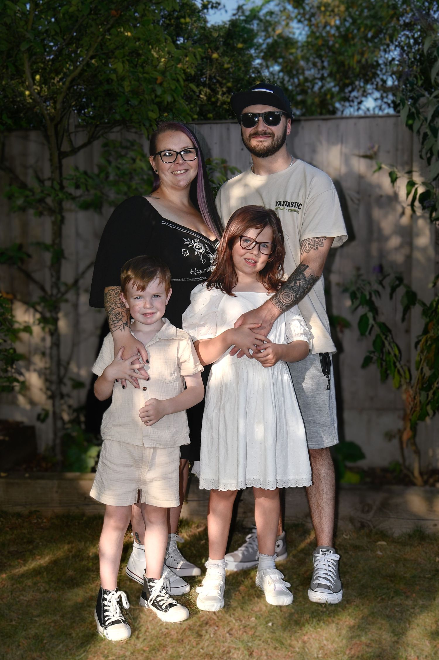 A family portrait taken outdoors against a garden wall in natural lighting.