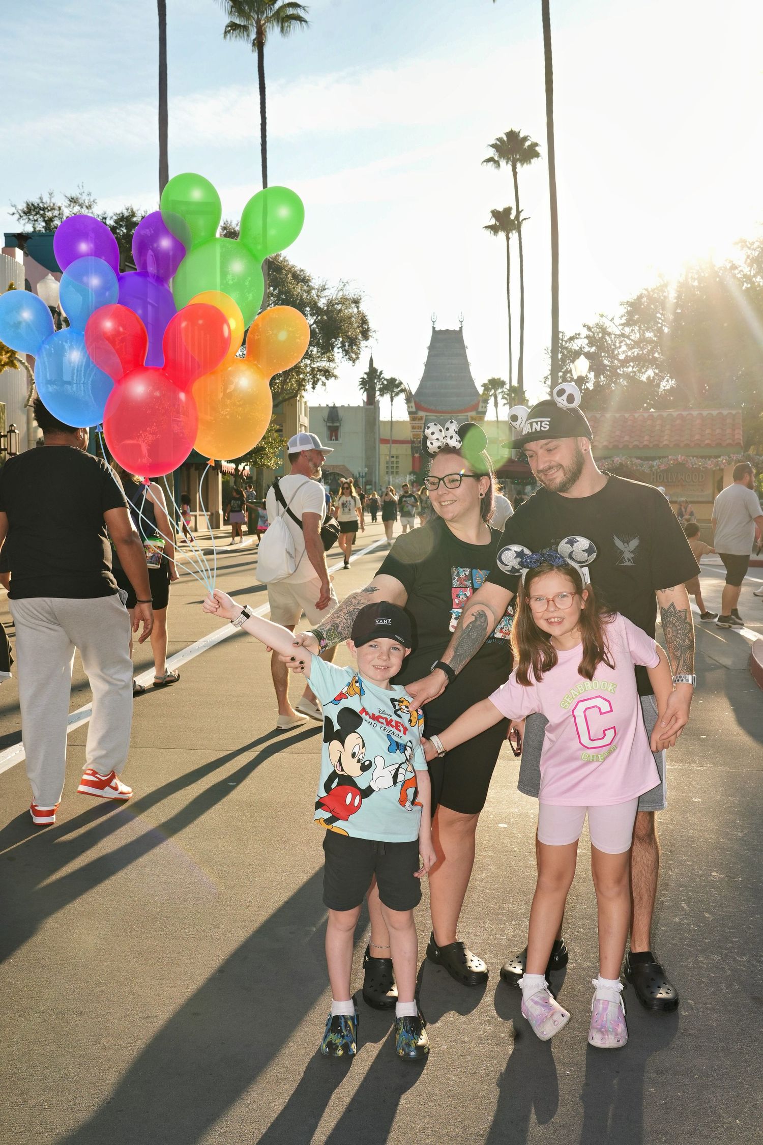 Happy family with colorful balloons walking along sunny palm-lined path.