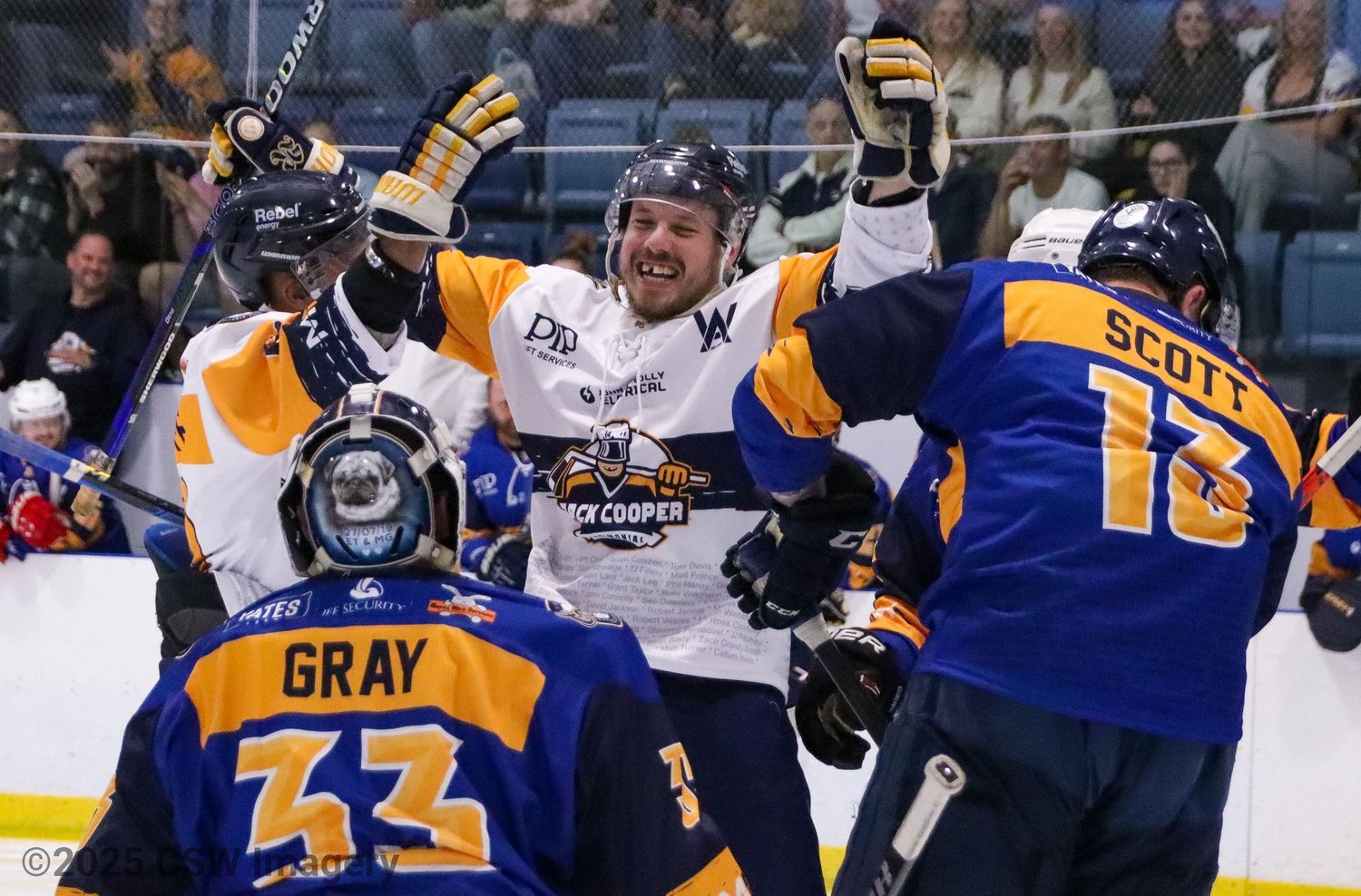 Hockey players in blue and orange jerseys celebrate during an intense game moment.