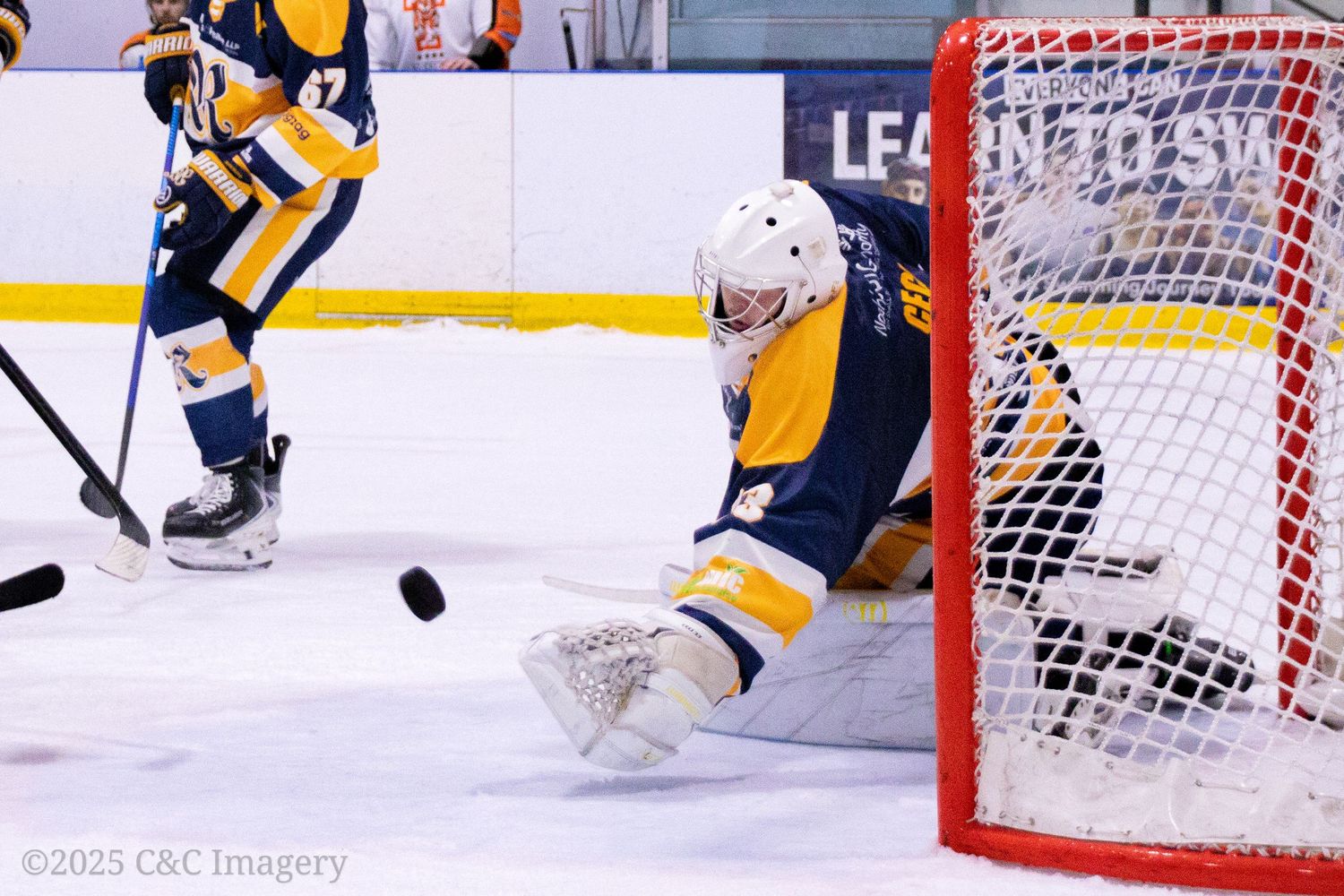 Hockey goalie makes a dramatic save during an intense NHL game with yellow and blue uniformed players.