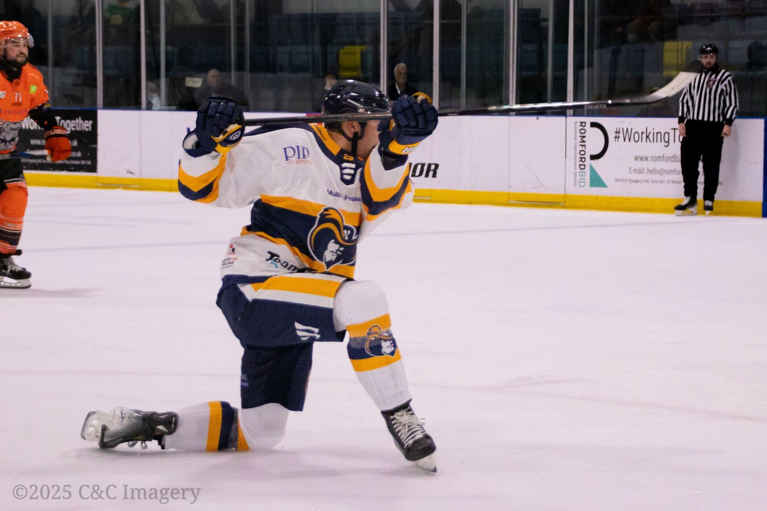 Ice hockey players compete in an intense match with players in orange and navy uniforms.