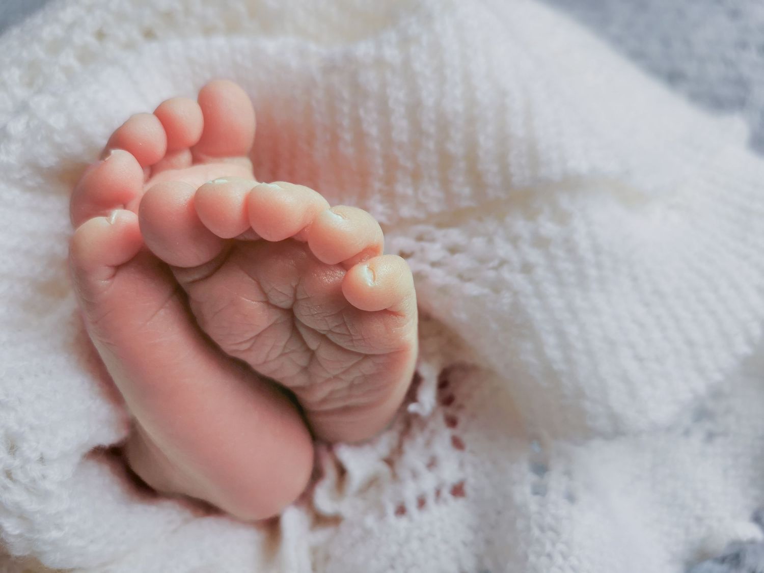 Close-up of tiny newborn baby feet peeking out from a soft white knit blanket.