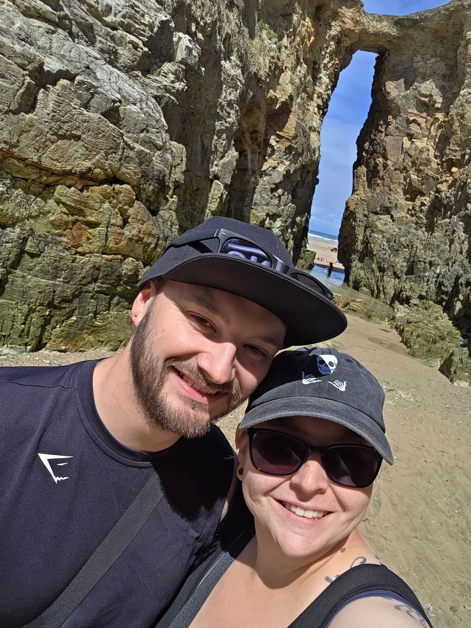 A couple takes a selfie in front of a dramatic rock formation with ocean views.