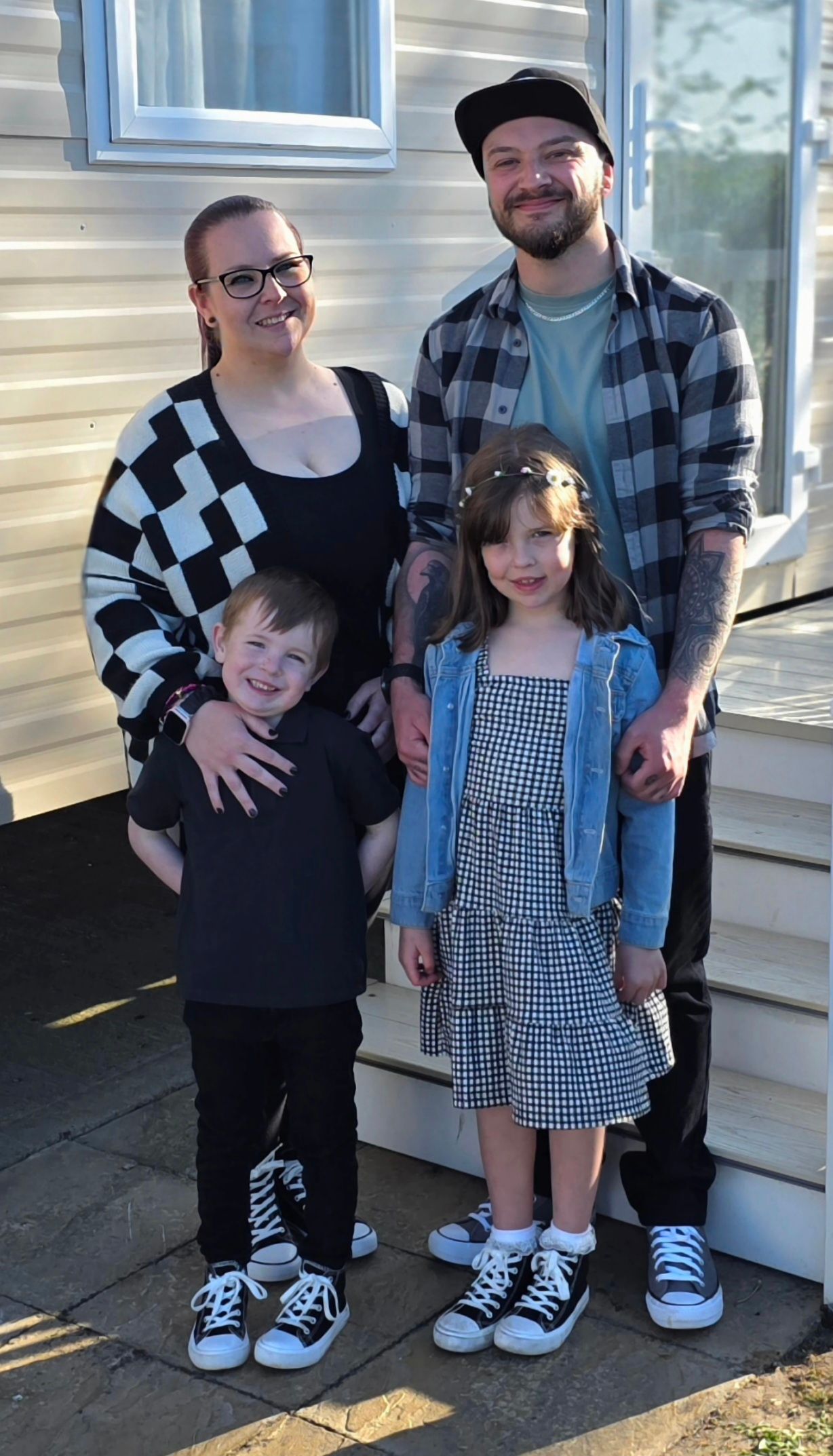 Family in coordinated black and white outfits posing together against white siding house.