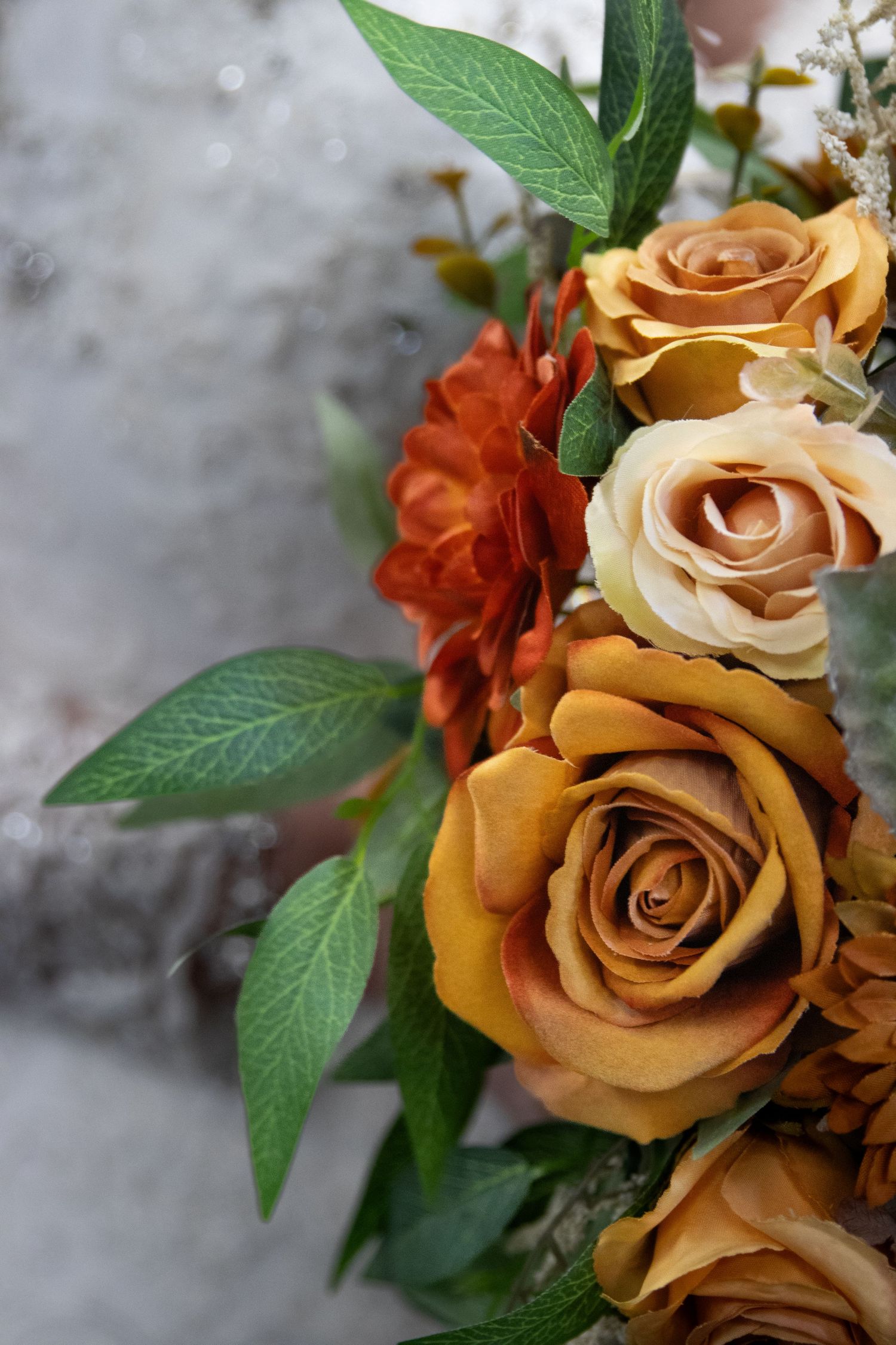 Close-up view of golden orange roses with green leaves against a misty gray background.