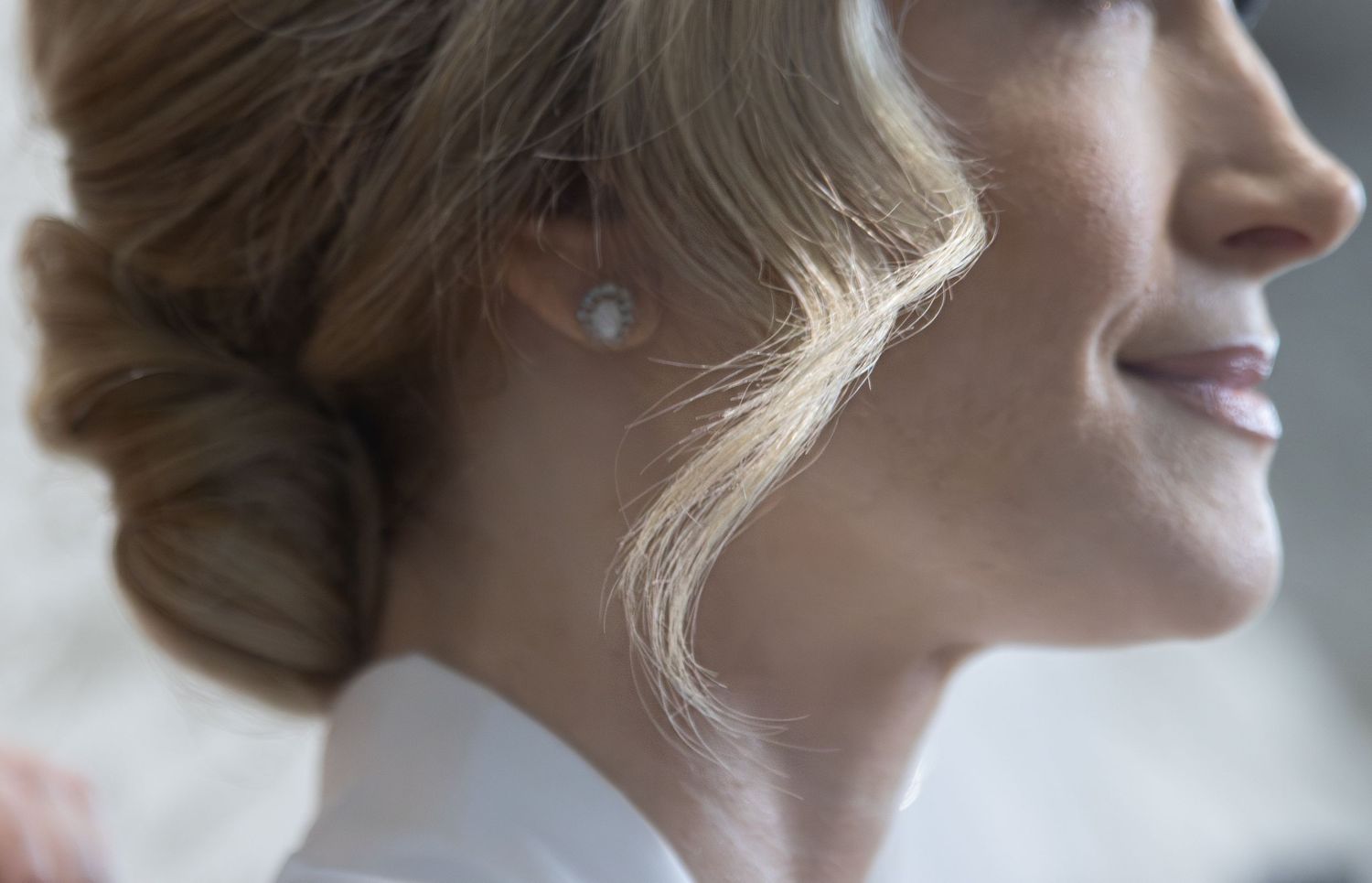 Elegant bride with pearl earring and updo hairstyle, smiling in profile view on her wedding day.