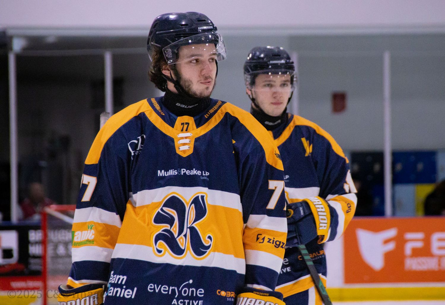 Hockey players in blue and yellow jerseys compete during an ice hockey match at an indoor arena.