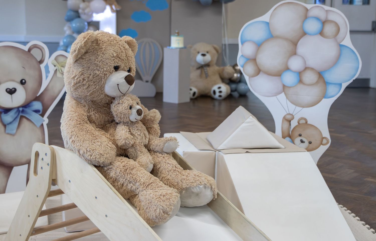 Two teddy bears sit on a wooden rocker slide at a blue teddy bear themed baby shower party decoration setup.