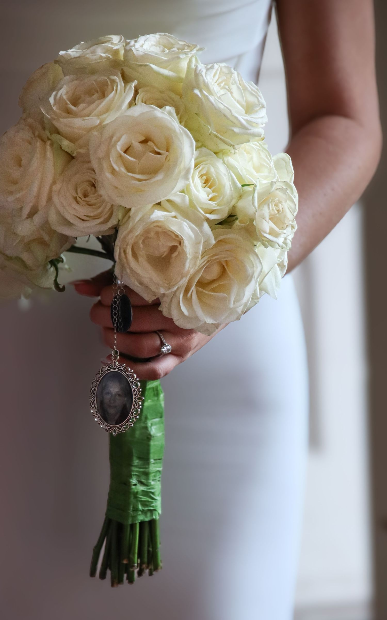 Bridal bouquet of white roses with vintage locket charm wrapped in green ribbon.
