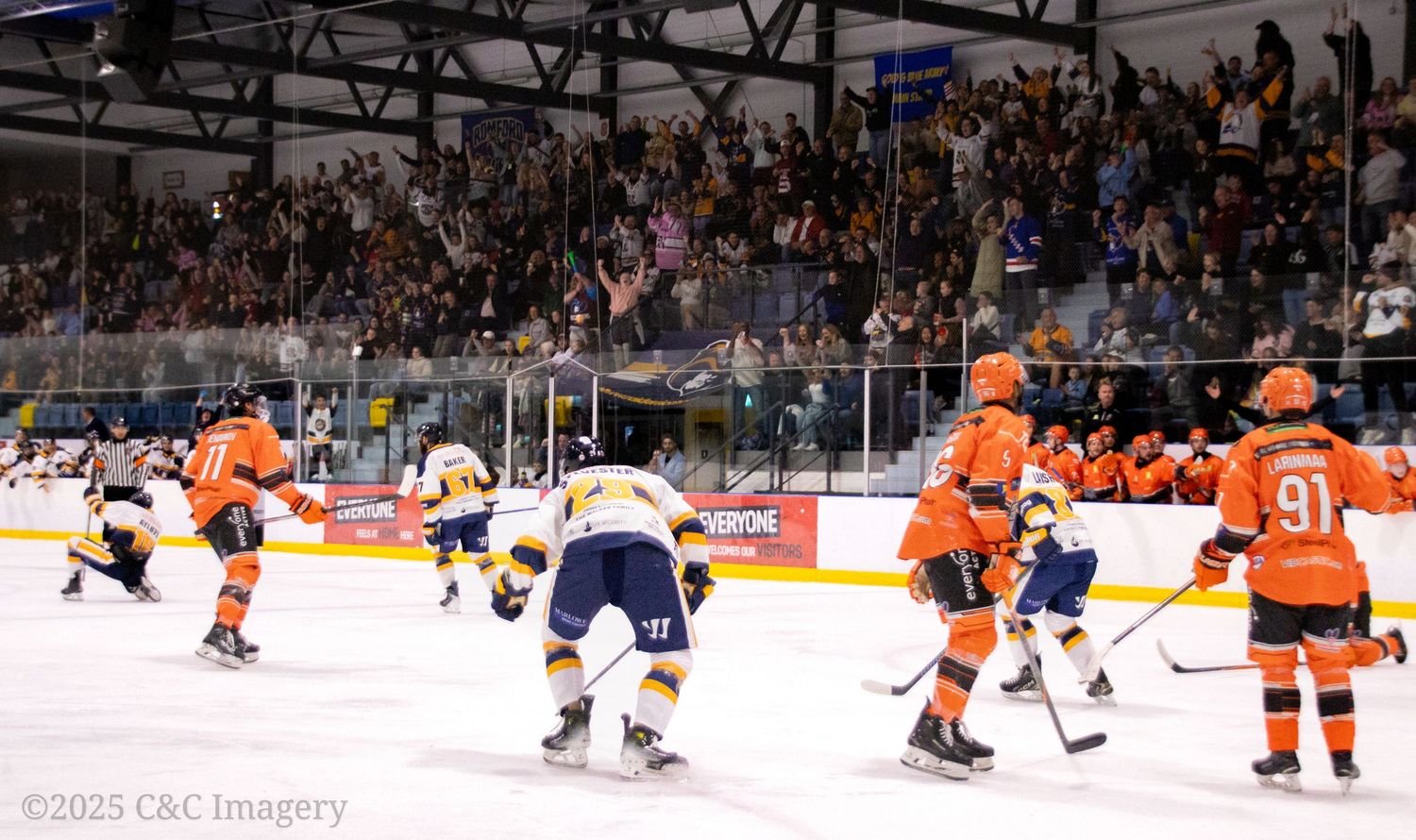 Hockey players in orange and blue jerseys compete during intense game action.
