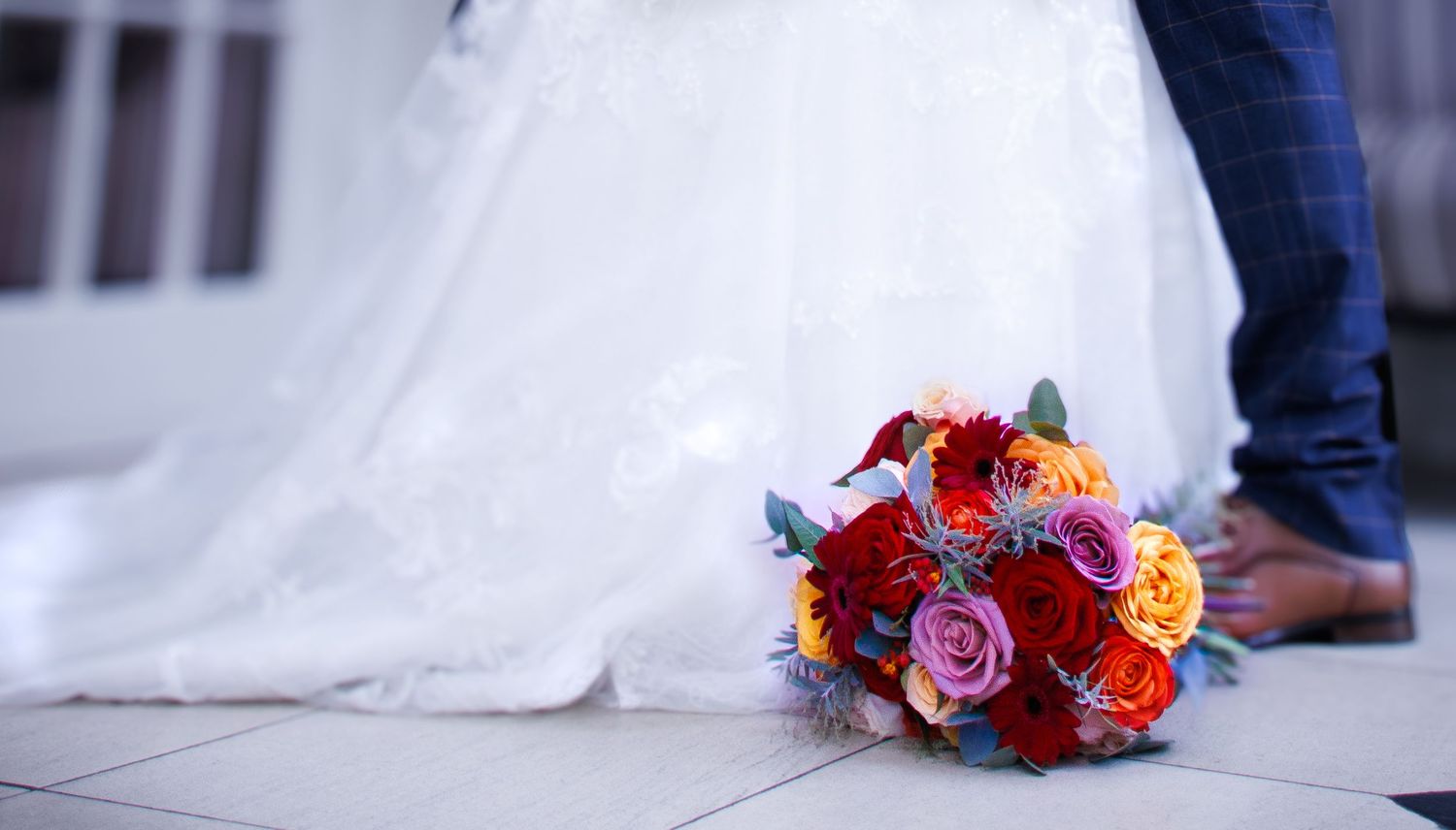 A vibrant wedding bouquet with red and orange flowers rests on a white surface.