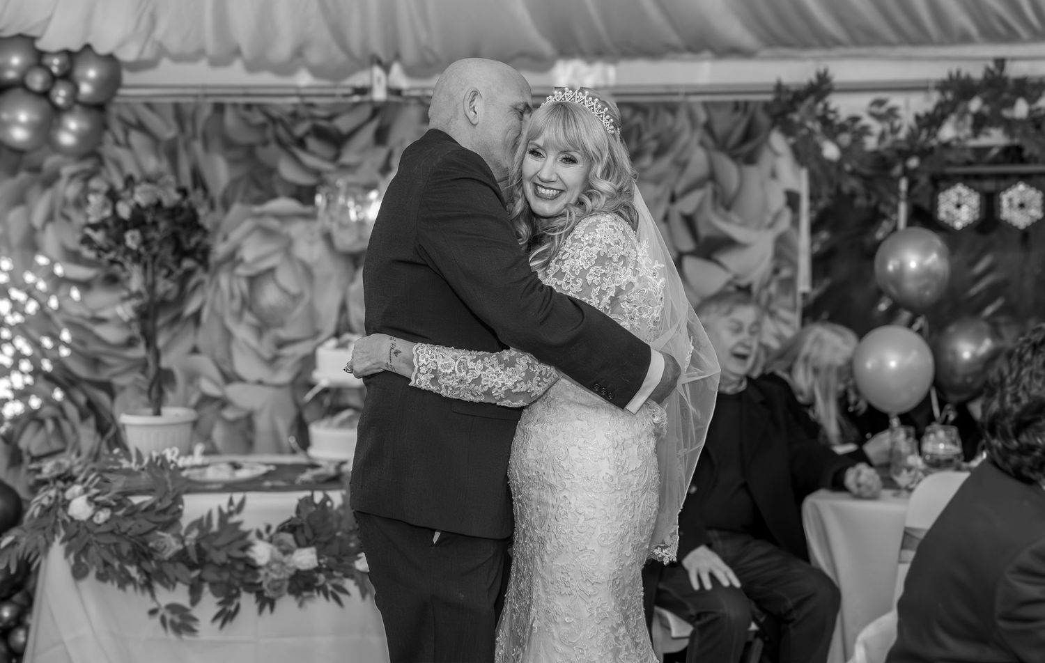 Couples dancing together at a wedding reception in a decorated venue with twinkling lights and floral arrangements.