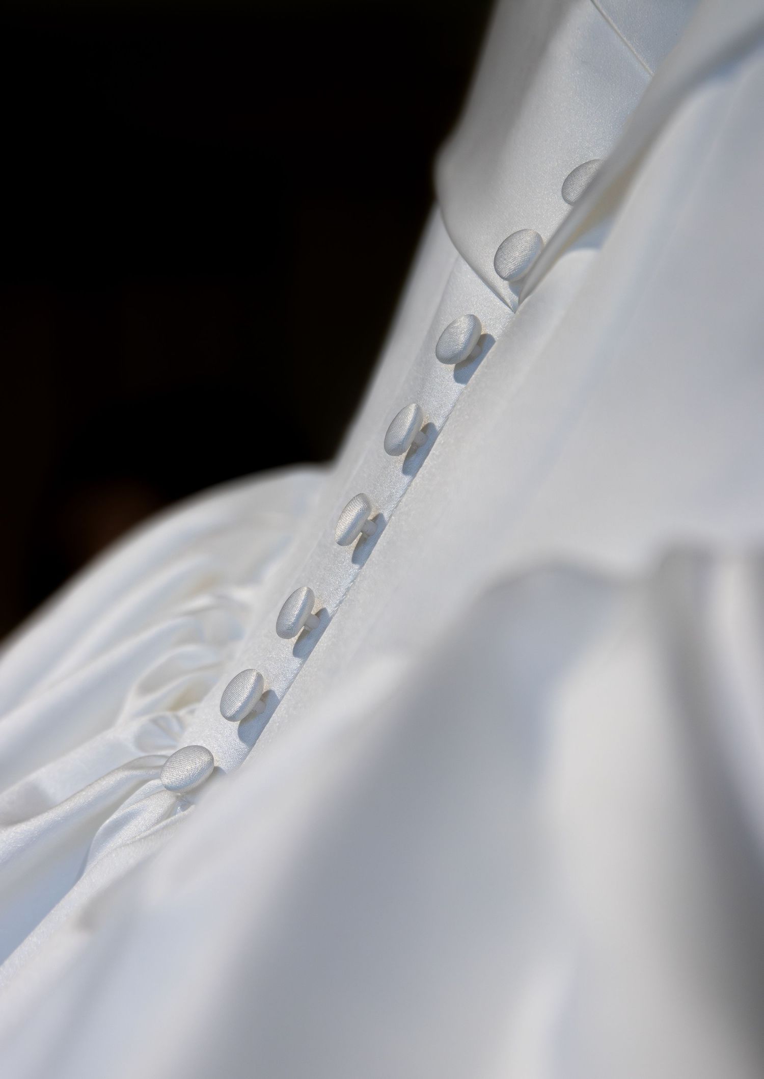 Close-up of elegant white wedding dress back with satin buttons and loop closures on silk fabric.