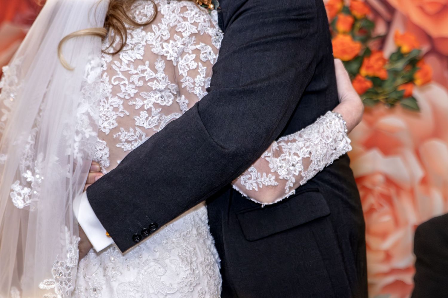 A couple in wedding attire embraces against a backdrop of orange autumn foliage during their outdoor ceremony.