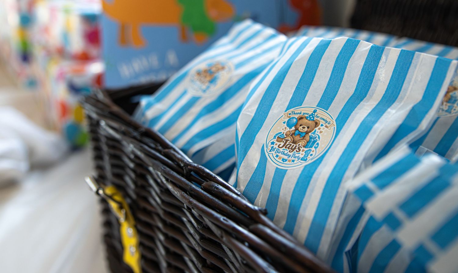 Blue and white striped gift bags with teddy bear logo displayed in a wicker basket at a children's store.