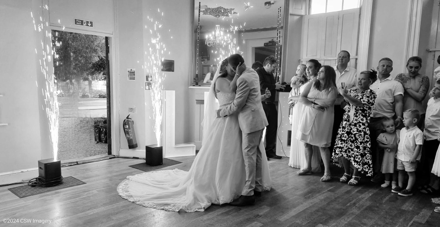 Black and white panorama of an indoor wedding reception with sparklers and guests.