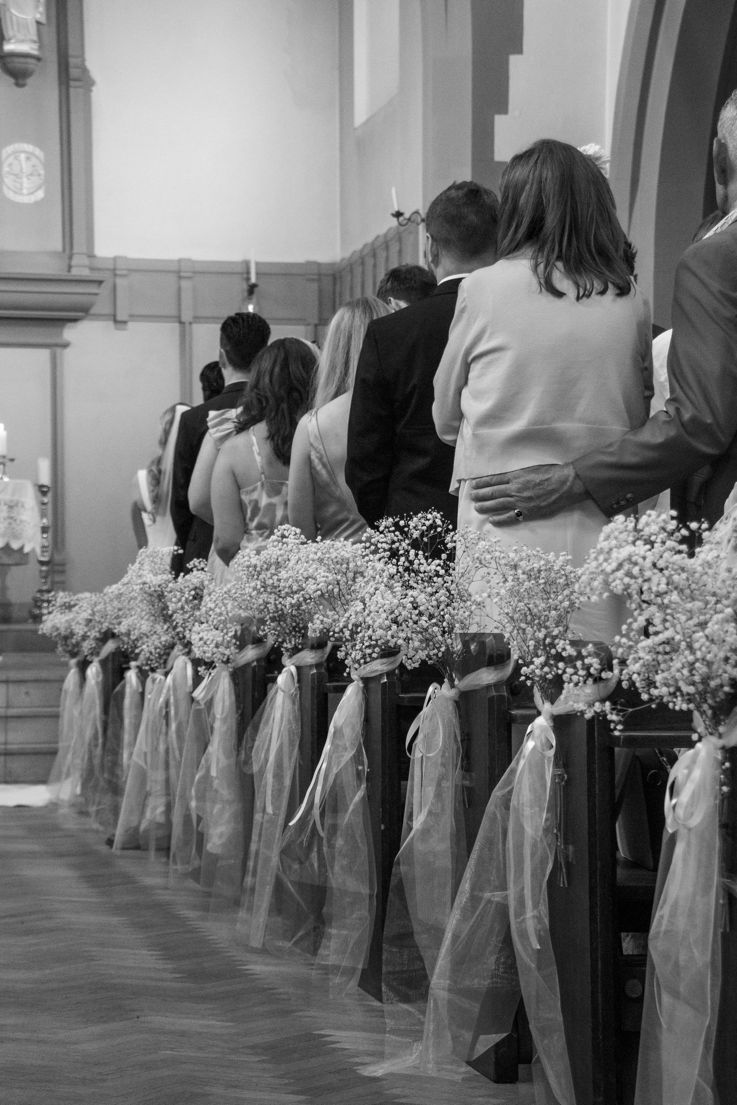 Church pews decorated with white flowers and purple ribbons for a wedding ceremony.