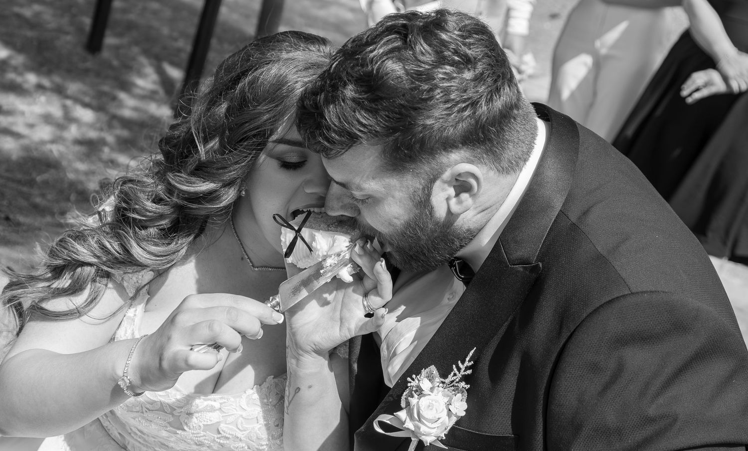 Black and white photo of bride and groom sharing wedding cake during reception ceremony.
