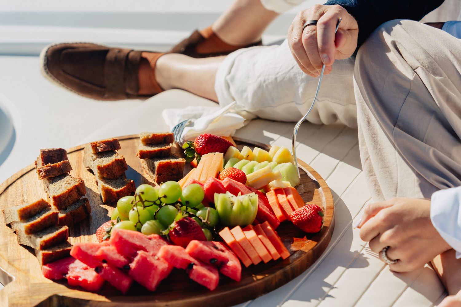 Charcuterie board with fresh fruit, cheese and snacks arranged on white surface.