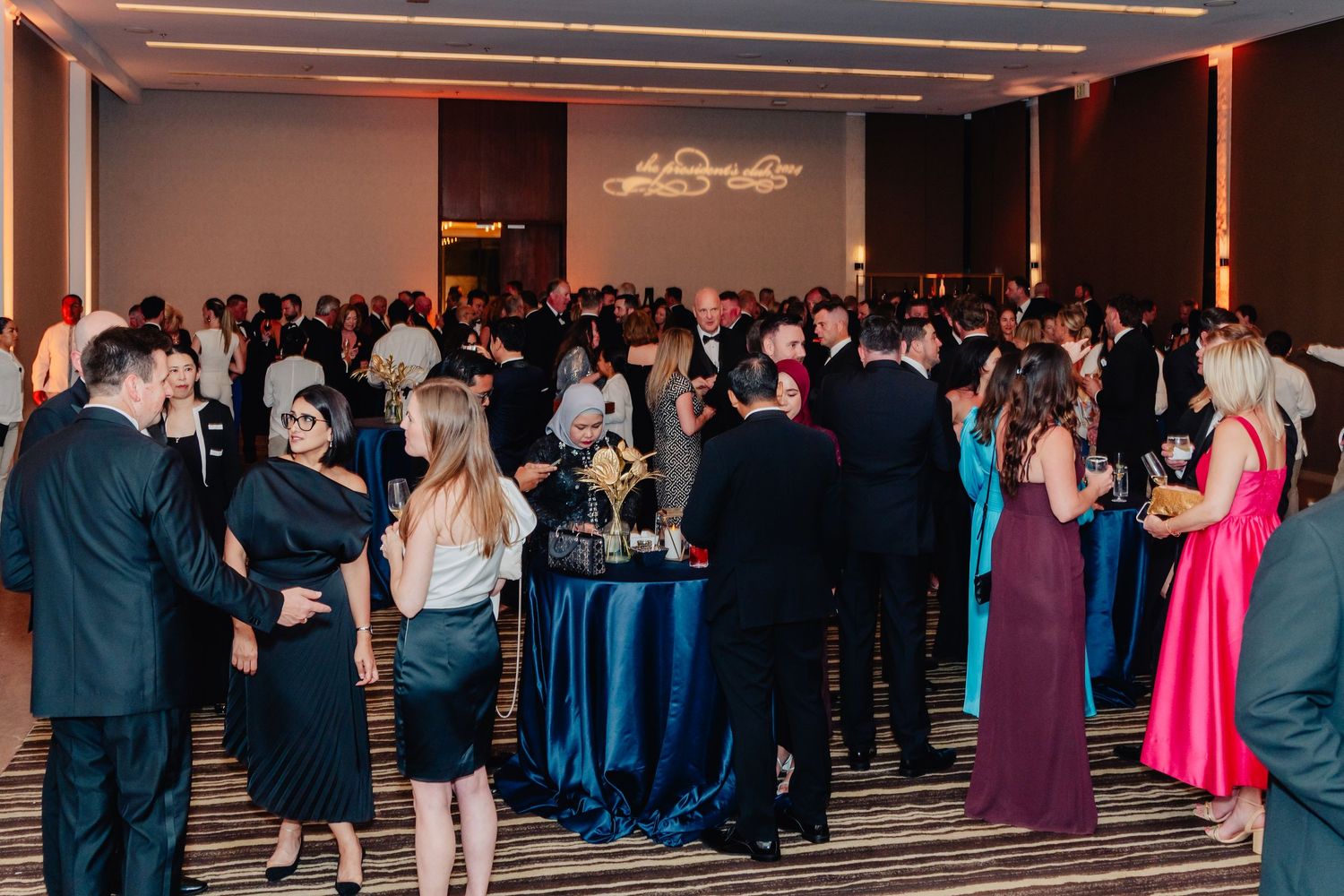 Large crowd mingling at formal event in dimly lit ballroom with ambient lighting.