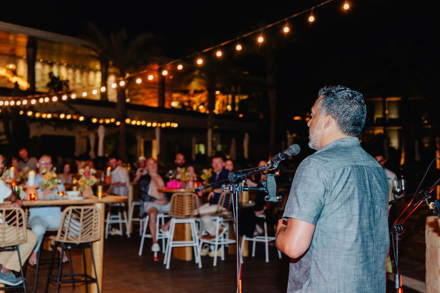 Performer with microphone entertains dining guests at an outdoor evening event.