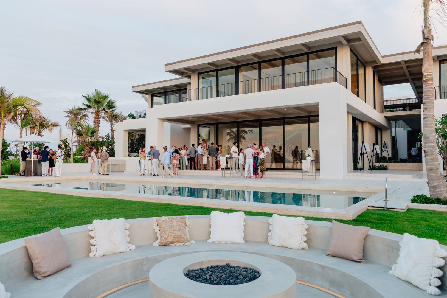 Luxury modern beachfront property with infinity pool and fire pit at sunset.