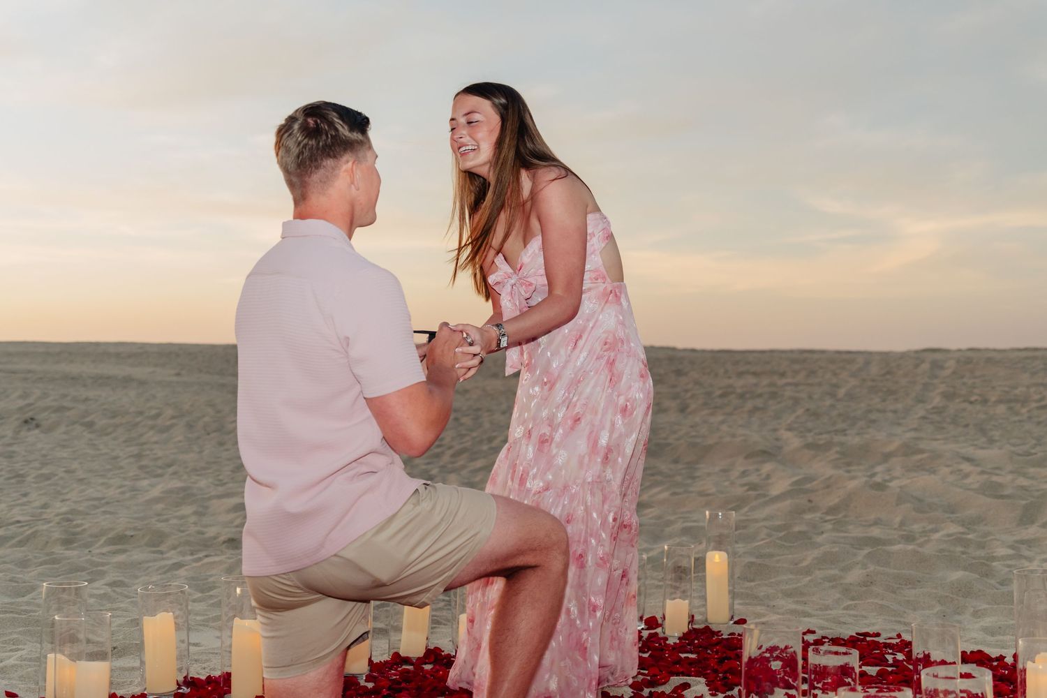 Couple sharing an intimate moment during beach proposal with candles and roses.