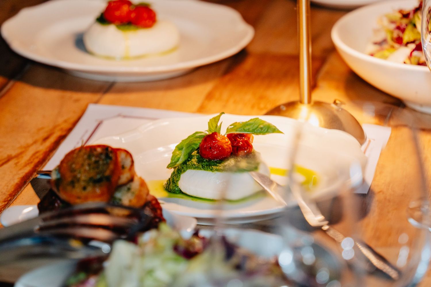 A series of elegant plated dishes with garnishes arranged on a wooden restaurant table in warm lighting.