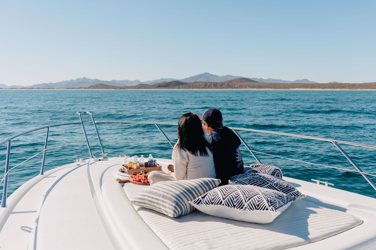 People relaxing on a luxury yacht deck while sailing across blue ocean waters with mountains visible in the distance.