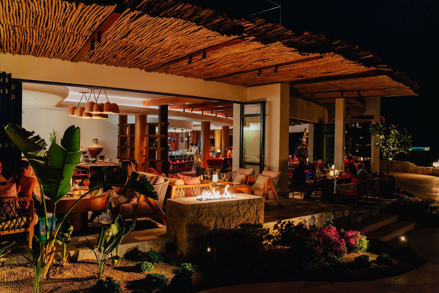 Cozy outdoor patio dining area at night with warm lighting and thatched roof creating an intimate tropical ambiance.