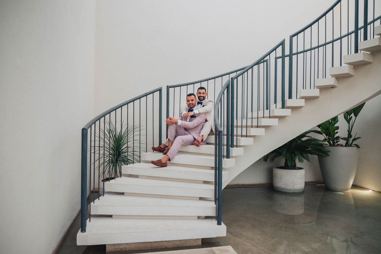 Two people in coordinated pink outfits sitting together on elegant white spiral stairs.