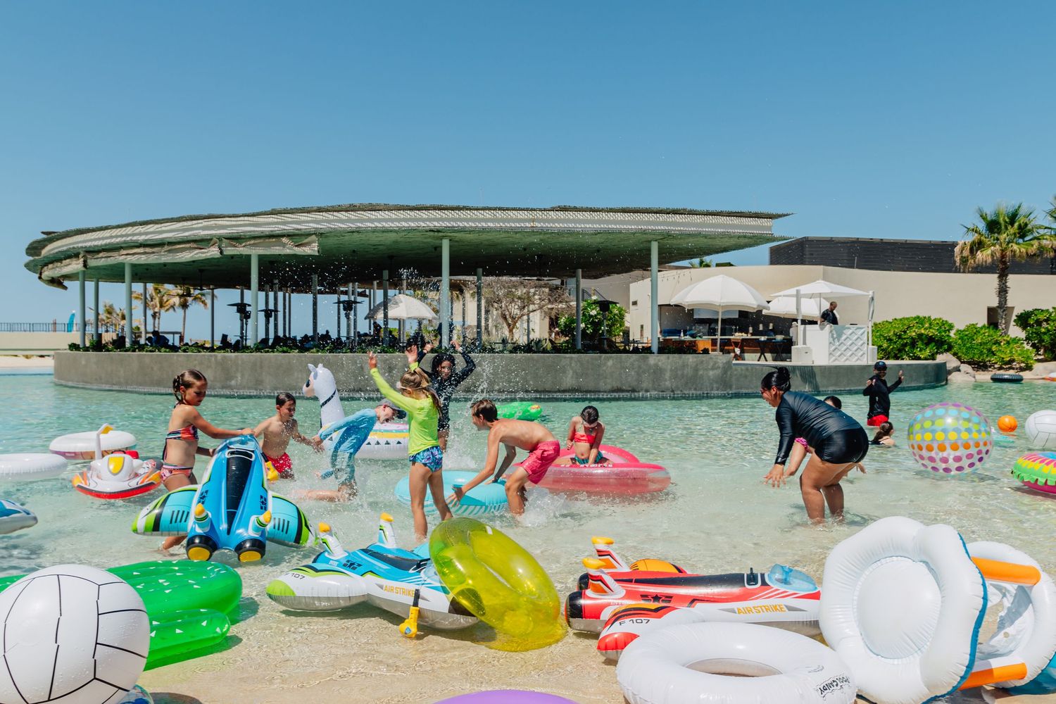 Beachfront recreation area with colorful pool floats and loungers on white sand.